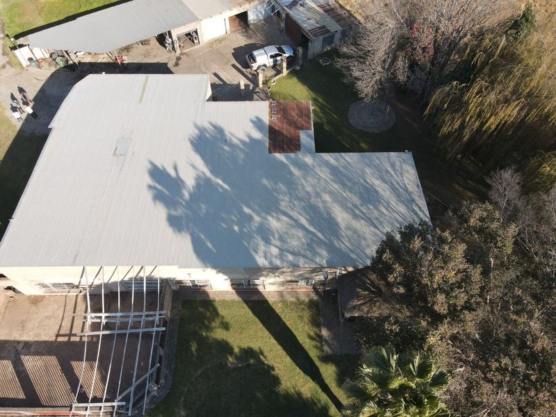 Aerial view of the small holding property showing the main dwelling with a metal roof, surrounding outbuildings, garden areas, and an unfinished pergola structure.