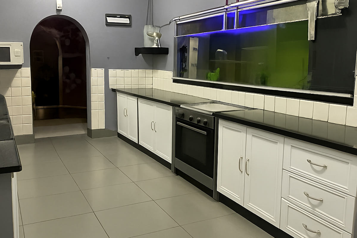 A clean, functional kitchen featuring white cabinetry, dark granite countertops, built-in oven, and tiled flooring, leading through an archway to an adjacent space.