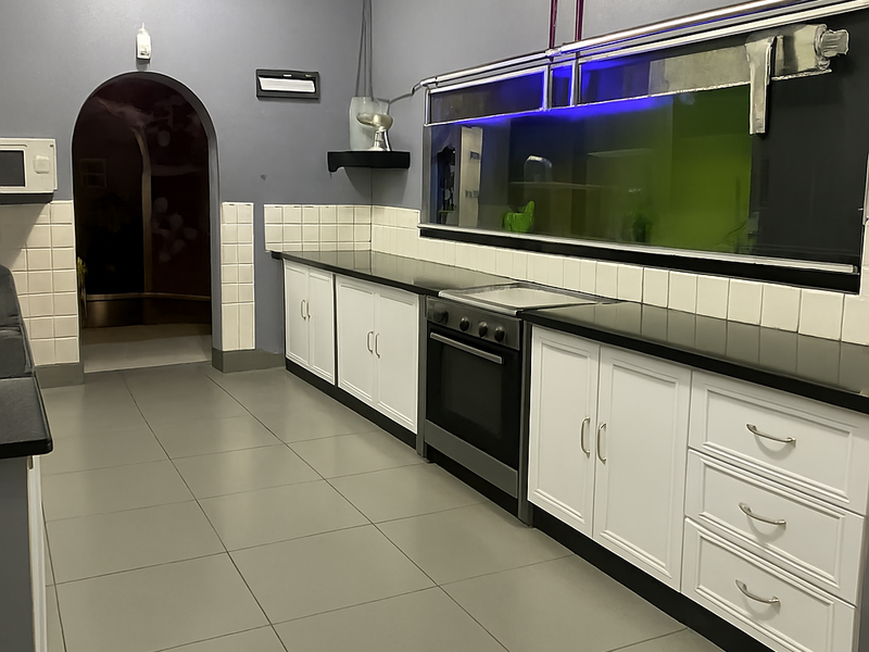A clean, functional kitchen featuring white cabinetry, dark granite countertops, built-in oven, and tiled flooring, leading through an archway to an adjacent space.