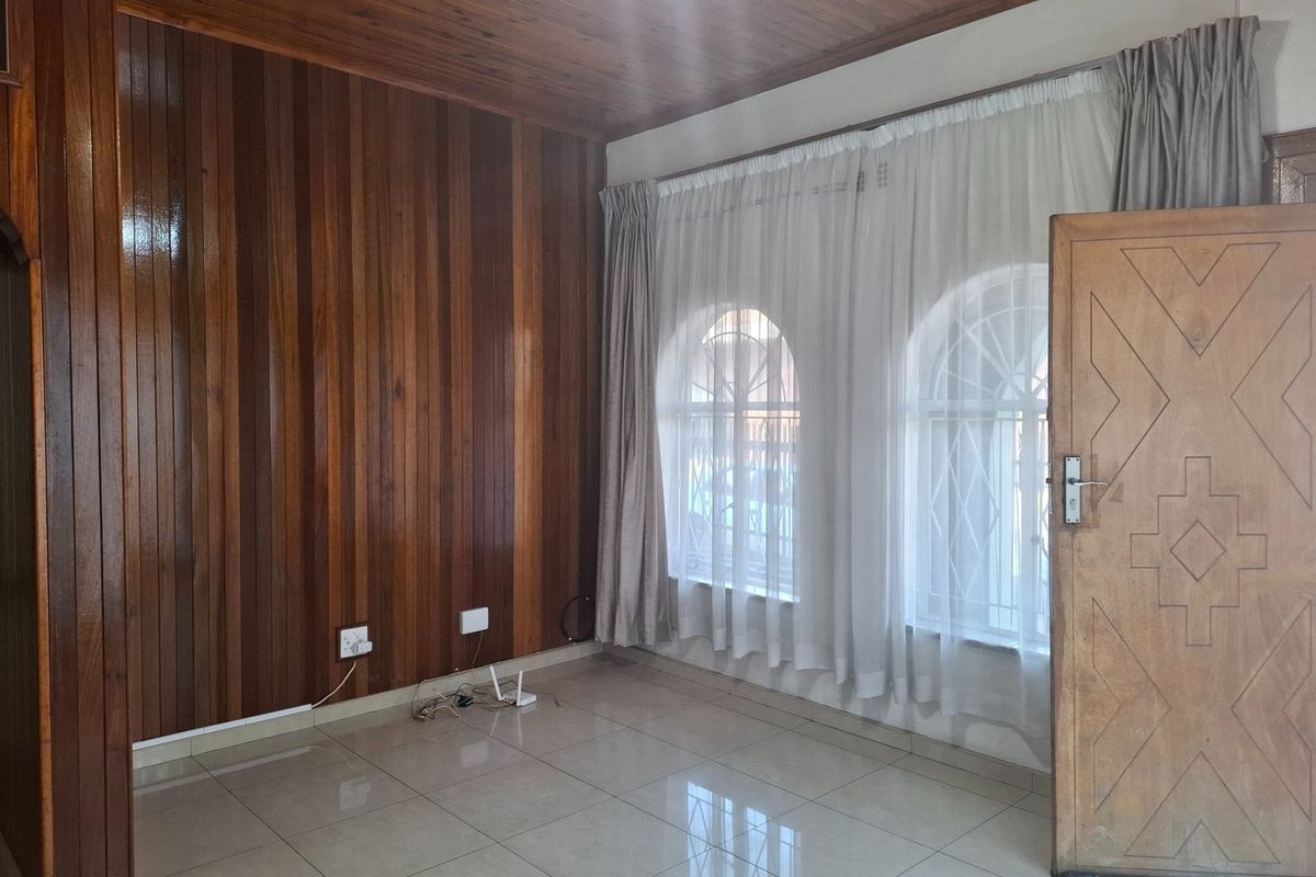 A bright, empty living room featuring polished timber wall paneling, a matching timber ceiling, tiled floors, and arched windows with security bars.