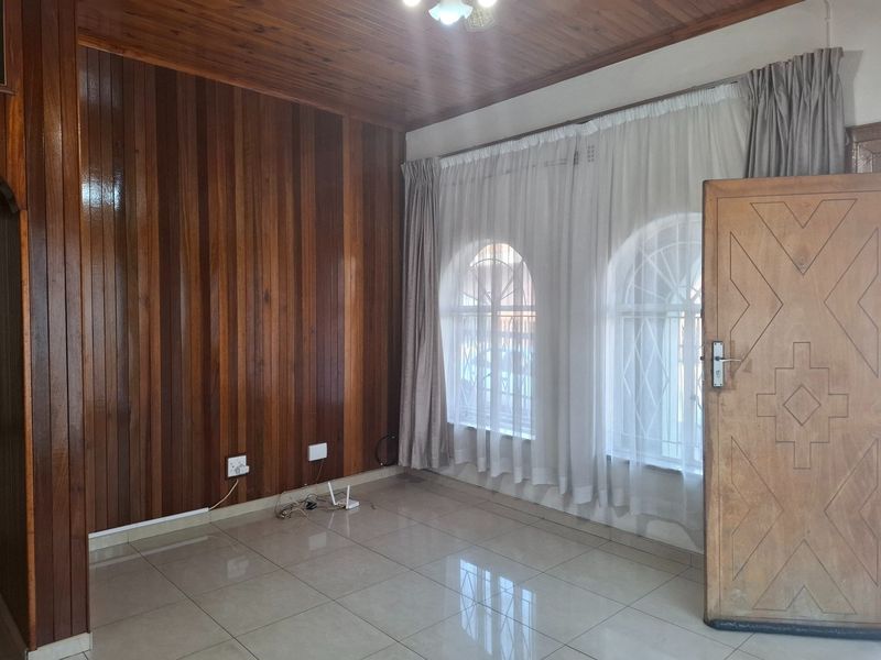A bright, empty living room featuring polished timber wall paneling, a matching timber ceiling, tiled floors, and arched windows with security bars.