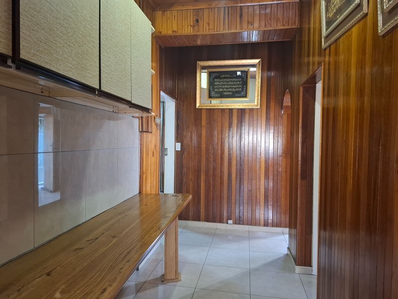 A kitchen area featuring extensive wooden wall and ceiling paneling, tiled flooring, and built-in wooden cabinetry and counter space.