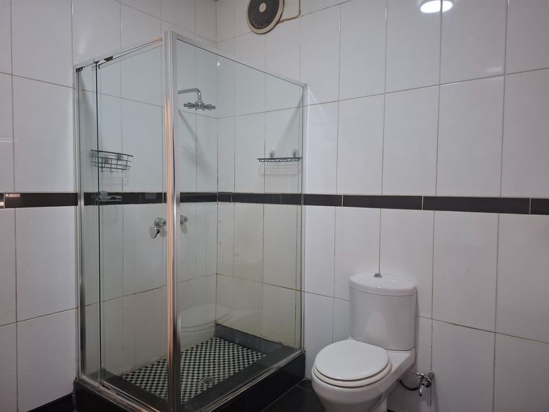 A functional bathroom featuring a glass-enclosed shower, white wall tiling with a dark accent border, and a standard toilet.