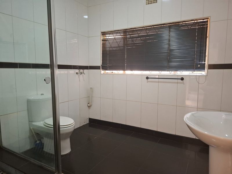 A functional bathroom featuring a glass shower enclosure, pedestal basin, toilet, and contrasting black and white tiled finishes.