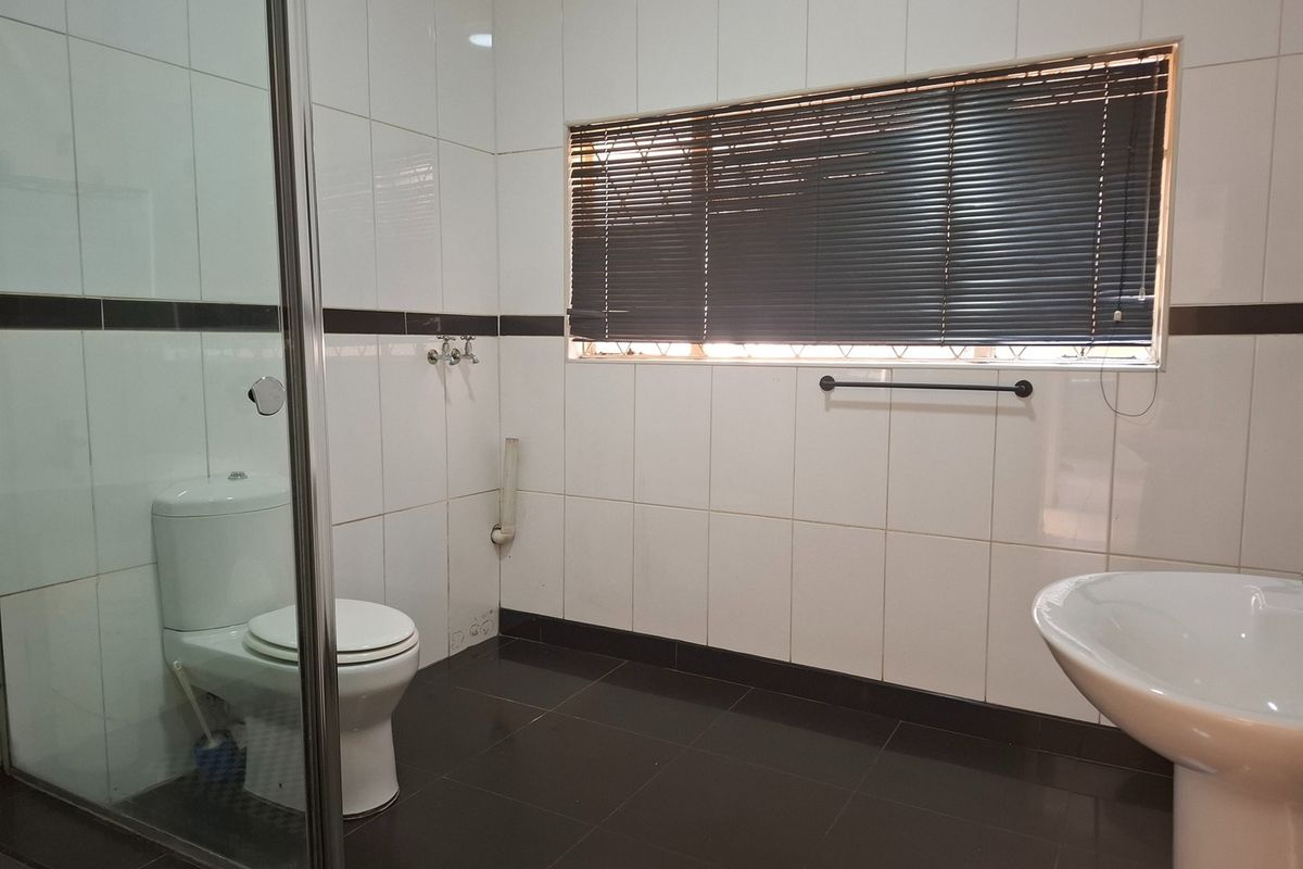 A functional bathroom featuring a glass shower enclosure, pedestal basin, toilet, and contrasting black and white tiled finishes.