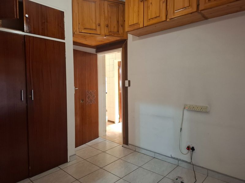 A bedroom featuring tiled flooring and extensive built-in wooden cabinetry, offering ample storage space and direct access to an adjoining room.