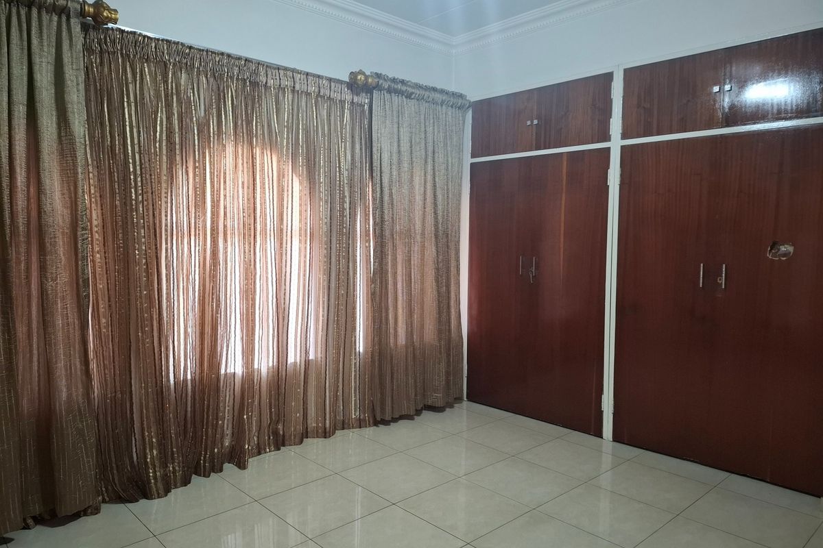 A clean, empty bedroom featuring tiled flooring, cornice detailing, and extensive built-in wooden cupboards providing ample storage space.