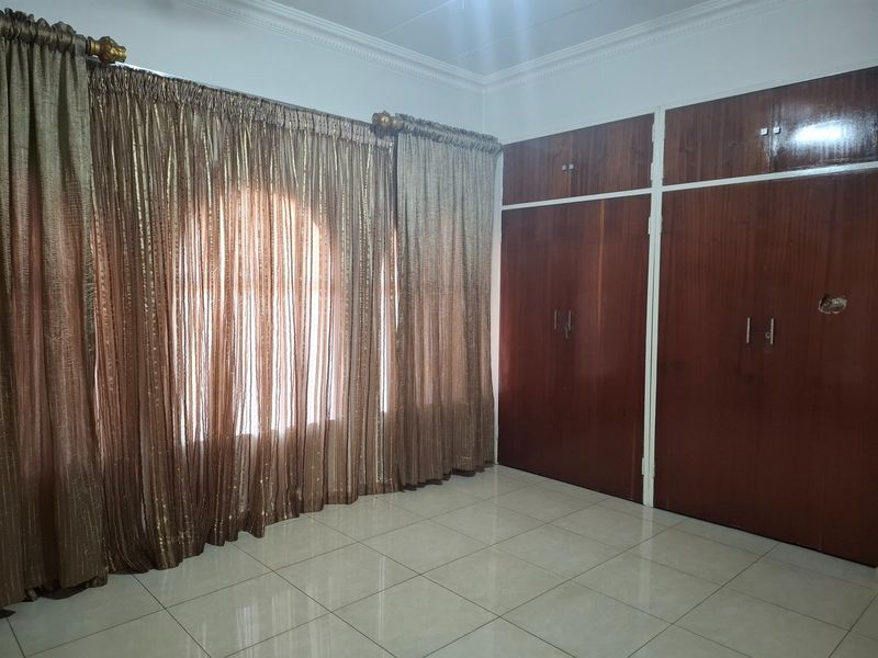 A clean, empty bedroom featuring tiled flooring, cornice detailing, and extensive built-in wooden cupboards providing ample storage space.