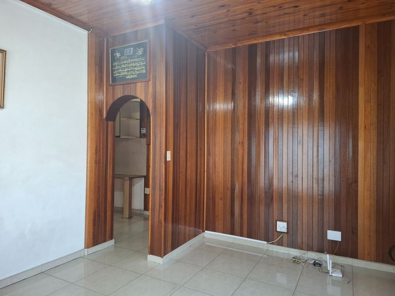 A living area featuring extensive timber wall paneling, a matching timber ceiling, and neutral tiled flooring with an arched transition to an adjacent space.