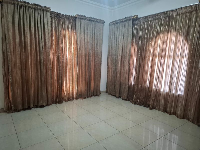 An empty living room featuring tiled flooring, decorative cornice, and large arched windows covered with floor-to-ceiling curtains.