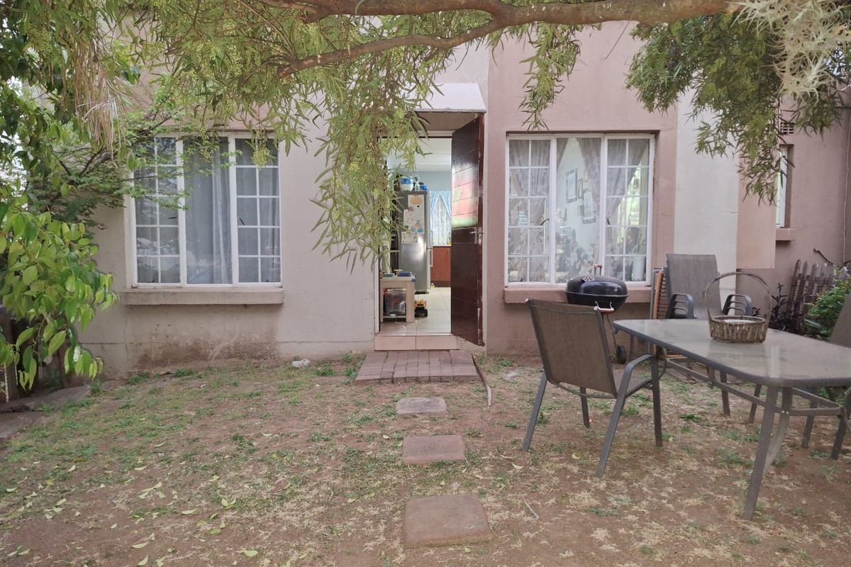 Rear view of the townhouse featuring a small garden area, brick pathway, and lattice windows leading into the interior living space.