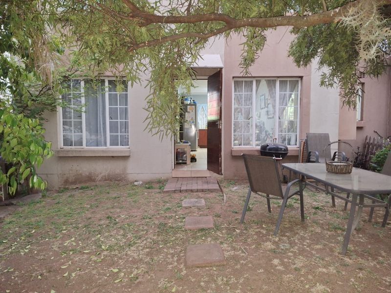 Rear view of the townhouse featuring a small garden area, brick pathway, and lattice windows leading into the interior living space.