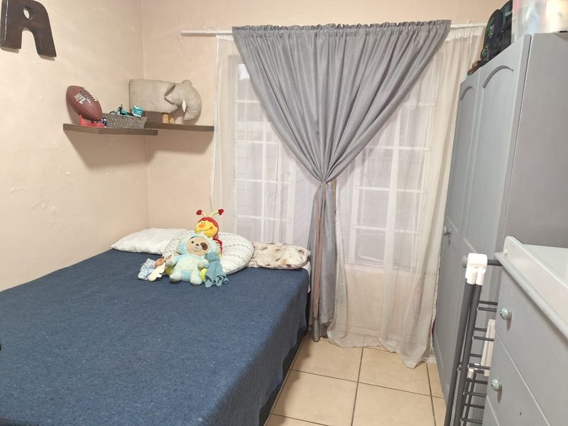 A compact bedroom featuring tiled flooring, a window with muntins, and wall-mounted floating shelves. The room requires minor cosmetic wall repairs.