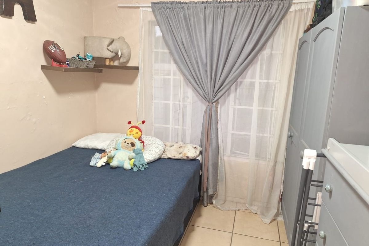 A compact bedroom featuring tiled flooring, a window with muntins, and wall-mounted floating shelves. The room requires minor cosmetic wall repairs.