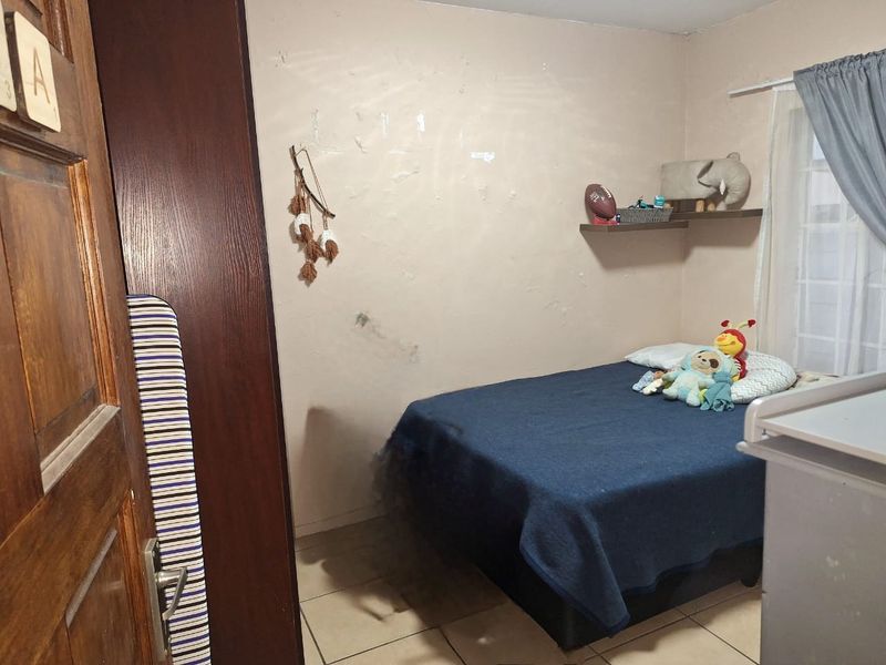 A bedroom featuring tiled flooring and a built-in cupboard, currently showing signs of wall surface wear and peeling paint.