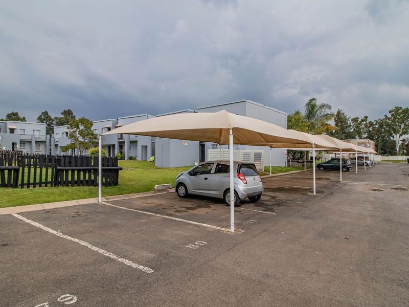 Exterior view of the townhouse complex featuring designated asphalt parking bays with shade cloth carports and perimeter fencing.