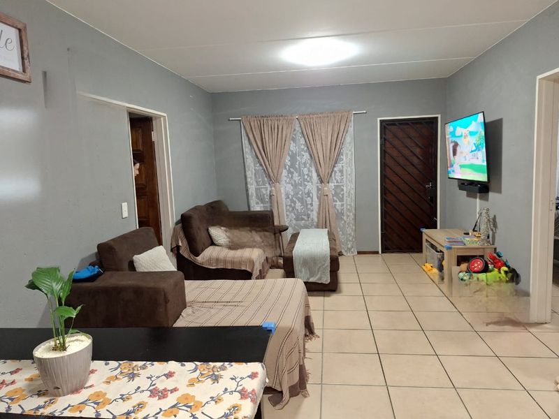 A living room featuring neutral grey walls, ceramic floor tiles, and a security gate entrance.