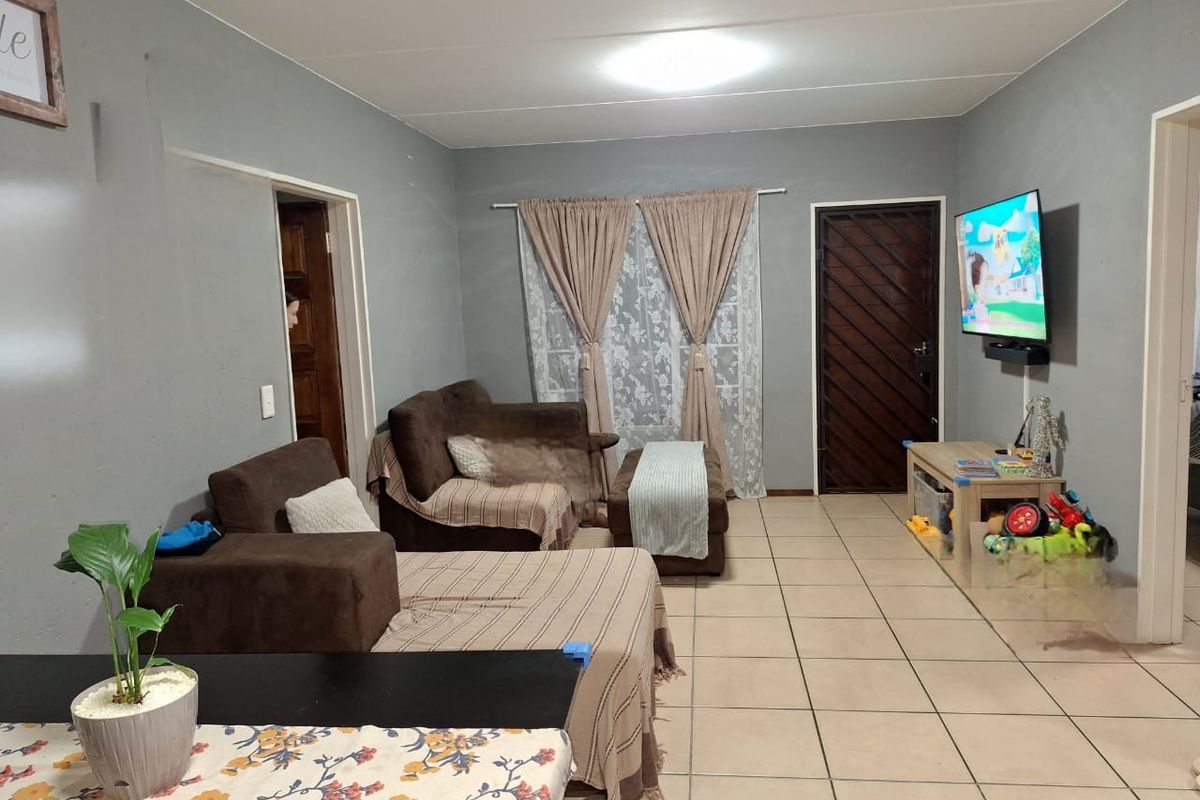 A living room featuring neutral grey walls, ceramic floor tiles, and a security gate entrance.