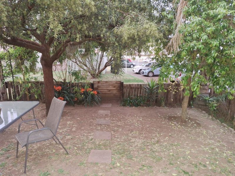 A private rear garden area featuring mature trees, a wooden boundary fence, and a stone pathway leading to the rear access point.