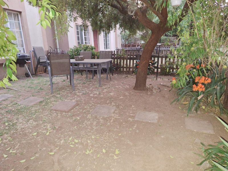 A rear garden area featuring a mature tree, paved stepping stones, and a timber picket fence, offering potential for landscaping and outdoor improvement.