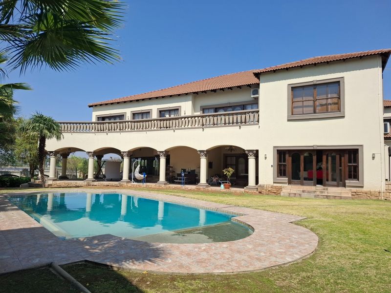 Spacious rear exterior featuring a swimming pool, covered patio with arched columns, and a large upper-level balcony with stone balustrades.