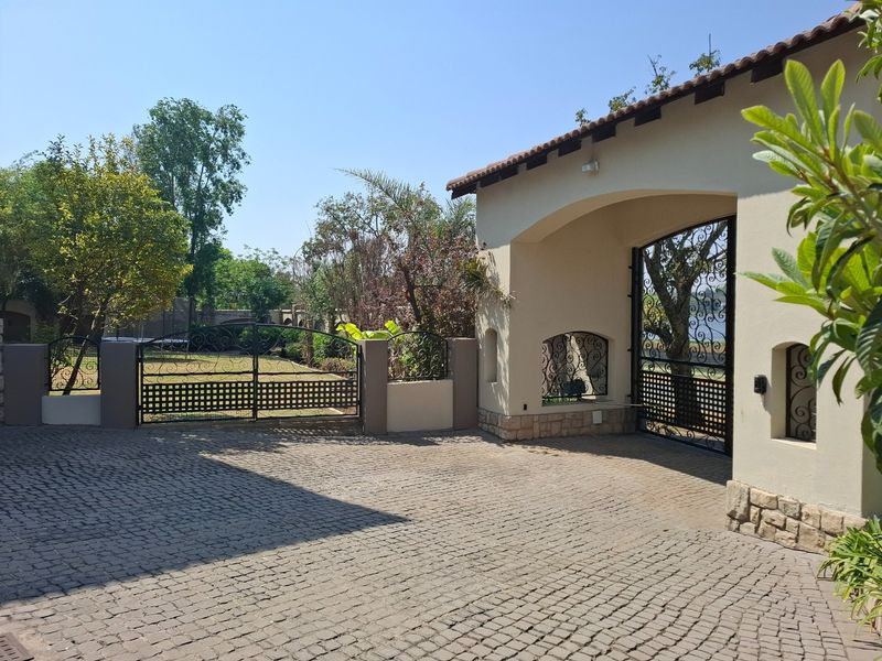 A well-maintained front entrance featuring a cobblestone driveway, decorative wrought iron gates, and stone-clad masonry pillars under a tiled roof.