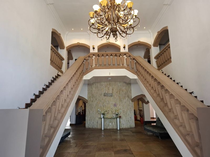 Grand entrance foyer featuring a symmetrical double staircase with stone balustrades, stone tile flooring, and an impressive central chandelier.