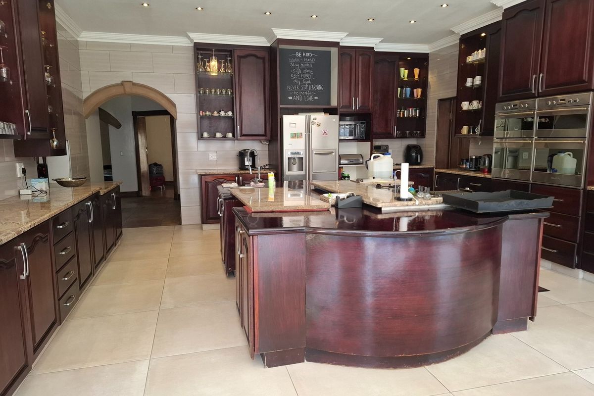Spacious kitchen featuring dark wood cabinetry, granite countertops, a large central island, and built-in double ovens with recessed lighting.
