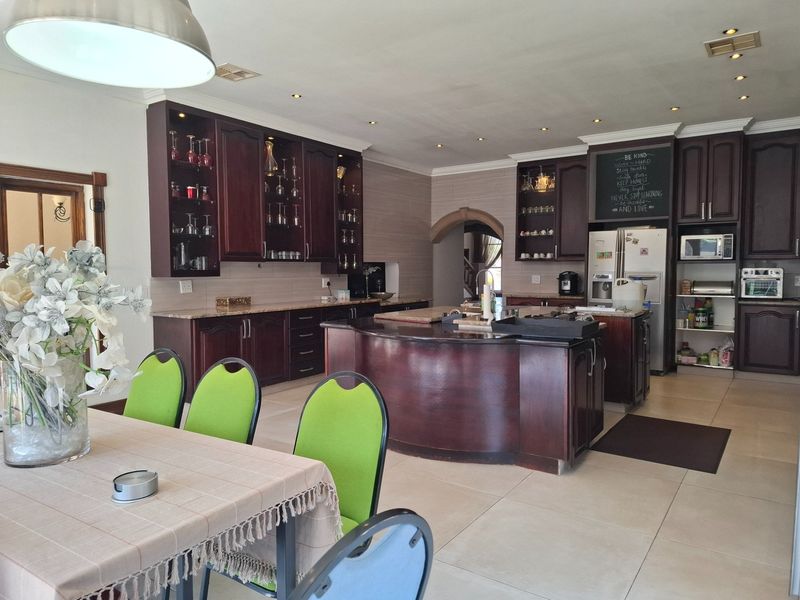 Spacious open-plan kitchen and dining area featuring dark wood cabinetry, granite countertops, a central kitchen island, and neutral tiled flooring.