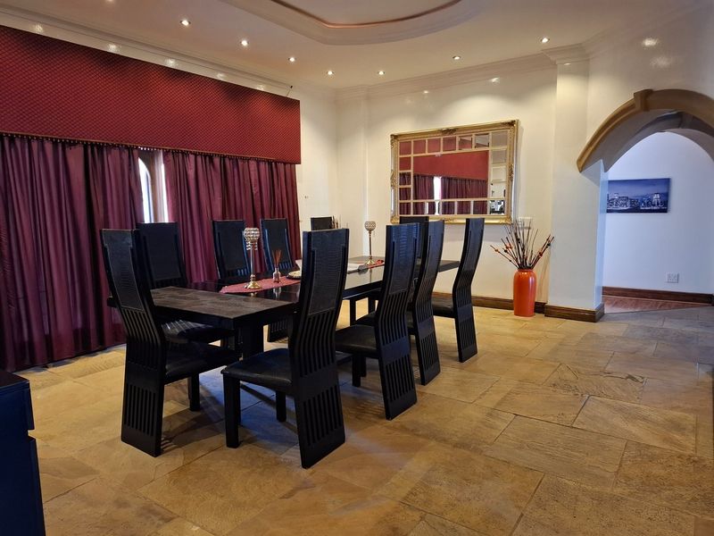 Spacious dining room featuring natural stone tile flooring, recessed ceiling lighting, and a distinctive arched entryway leading to adjacent living areas.