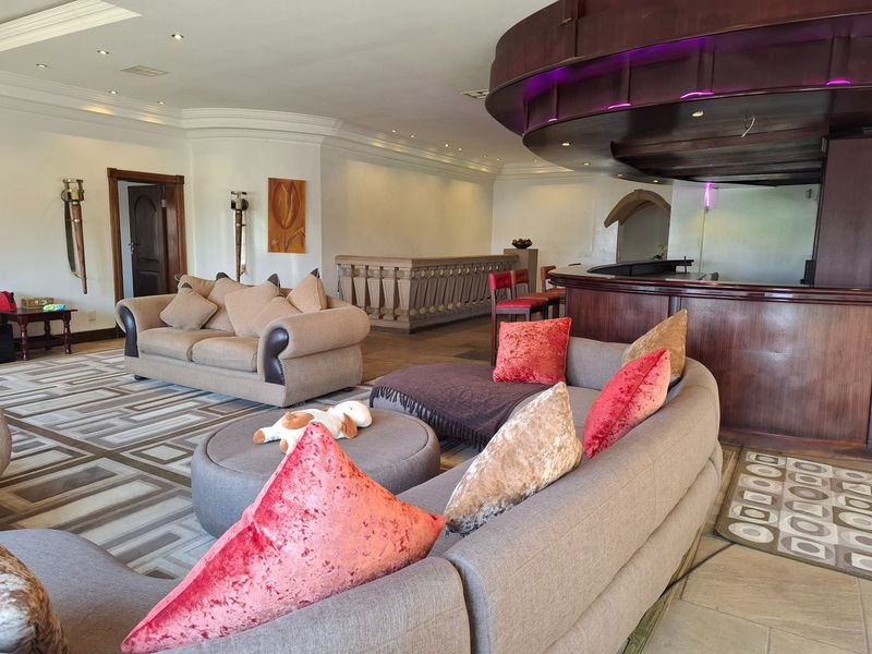 Spacious entertainment area featuring a large built-in bar with decorative bulkhead lighting, stone balustrade detailing, and tiled flooring throughout.