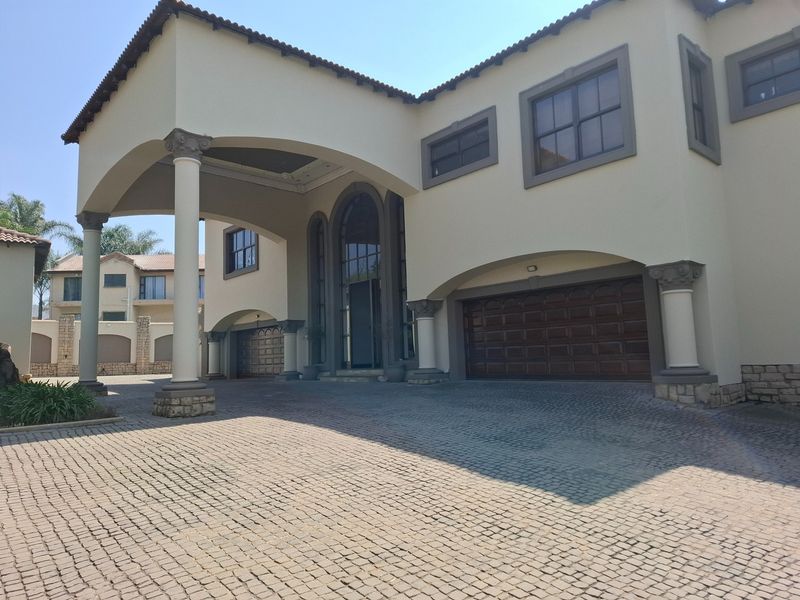 A grand front elevation featuring a spacious cobblestone driveway, covered portico entrance, and integrated double garage doors with classic architectural detailing.
