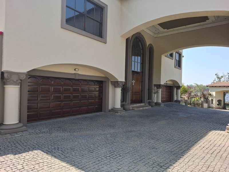 Impressive front facade featuring a grand arched portico, decorative columns, and a spacious cobblestone driveway leading to a double garage.