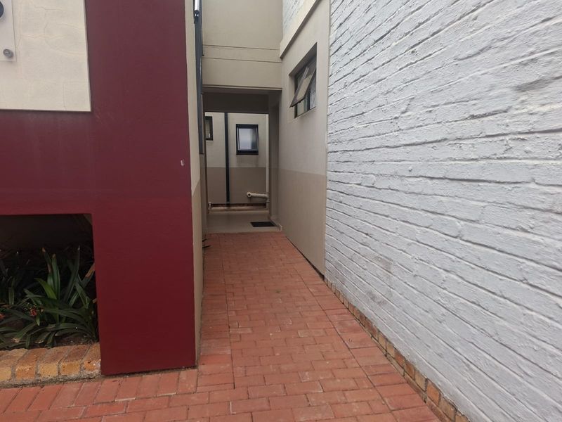 A narrow exterior side passage featuring brick paving, painted brick walls, and a small casement window, providing access to the rear of the townhouse.