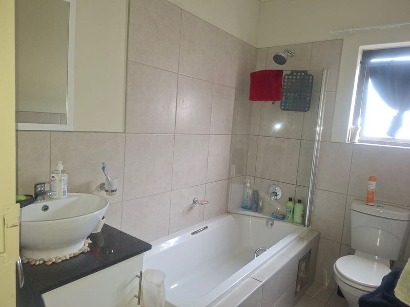 A functional bathroom featuring a vessel sink on a granite vanity, a built-in bathtub with a glass shower screen, and a standard toilet.