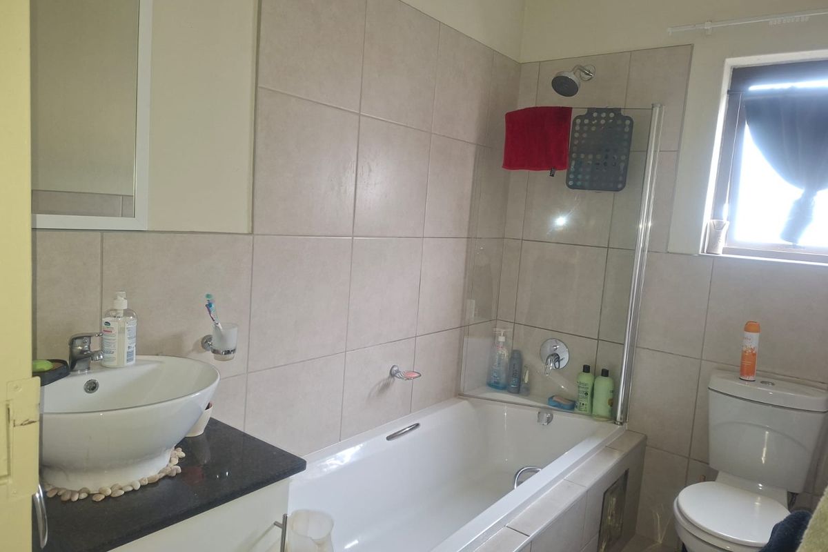 A functional bathroom featuring a vessel sink on a granite vanity, a built-in bathtub with a glass shower screen, and a standard toilet.