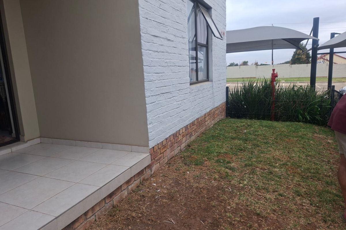 A view of the rear exterior featuring a tiled patio area, brick and painted facade, and a small garden space with shade sail structure.