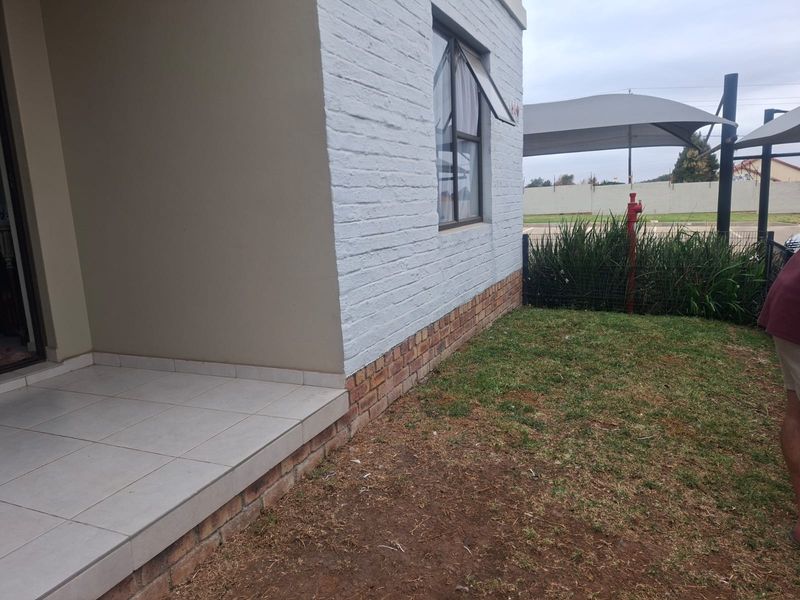 A view of the rear exterior featuring a tiled patio area, brick and painted facade, and a small garden space with shade sail structure.