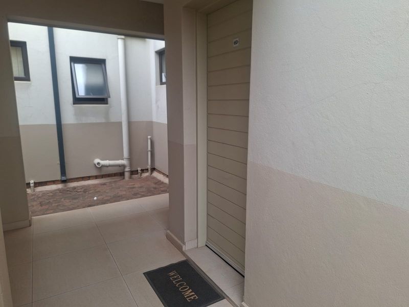 A clean and functional townhouse entrance area featuring tiled flooring and a secure external door leading to a small courtyard space.