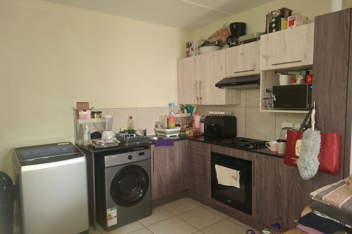 Compact kitchen featuring wood-look cabinetry, built-in oven, gas hob, extractor fan, and integrated laundry appliance space with tiled flooring and backsplash.