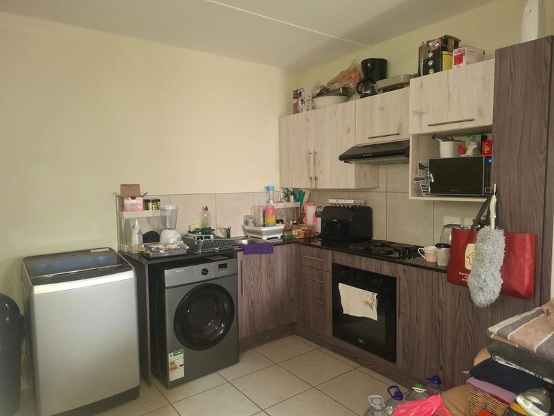 Compact kitchen featuring wood-look cabinetry, built-in oven, gas hob, extractor fan, and integrated laundry appliance space with tiled flooring and backsplash.