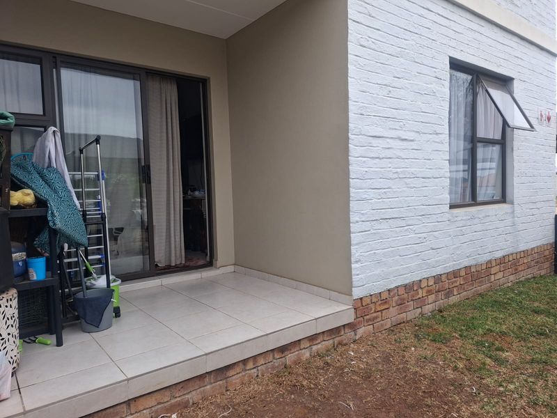 A covered patio area featuring tiled flooring, a sliding glass door entrance, and a white painted brick exterior wall.