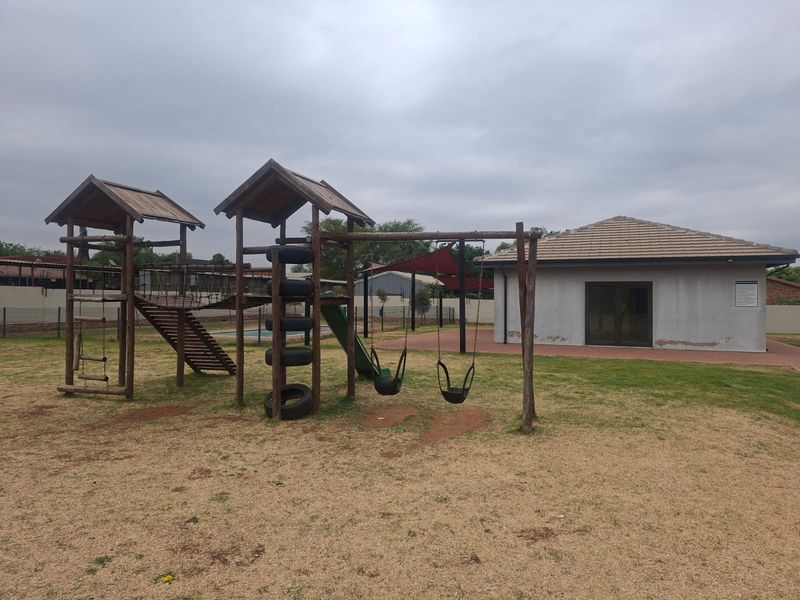 Communal area featuring a playground and a clubhouse building with a tiled roof and paved patio access.