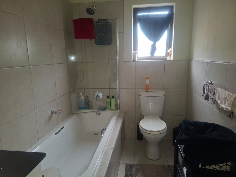 A functional bathroom featuring a bathtub with a shower head, glass screen, and a standard toilet, finished with neutral wall and floor tiles.