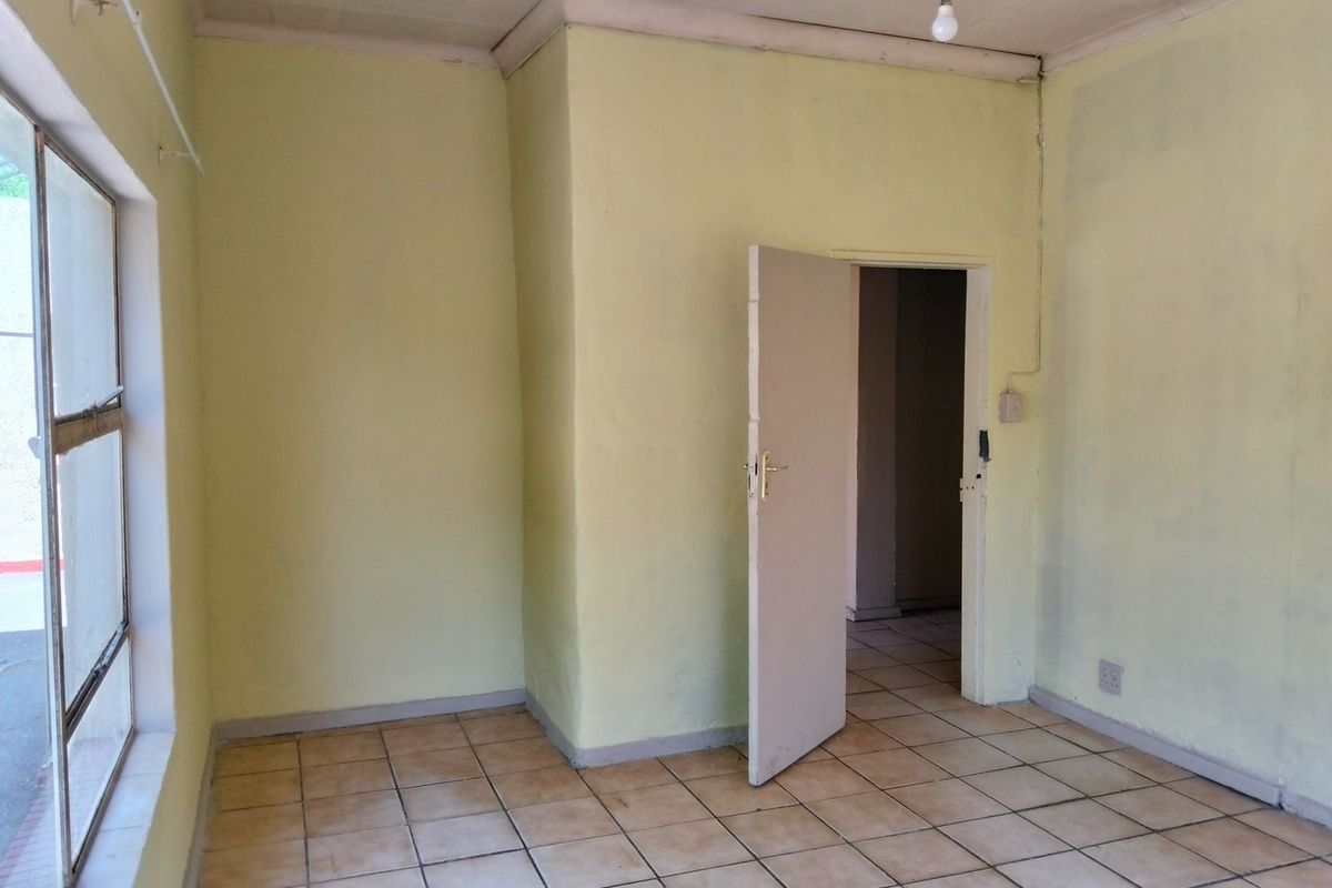 An empty bedroom featuring ceramic floor tiles, coved ceilings, and a single-pane window, offering a blank canvas for renovation.