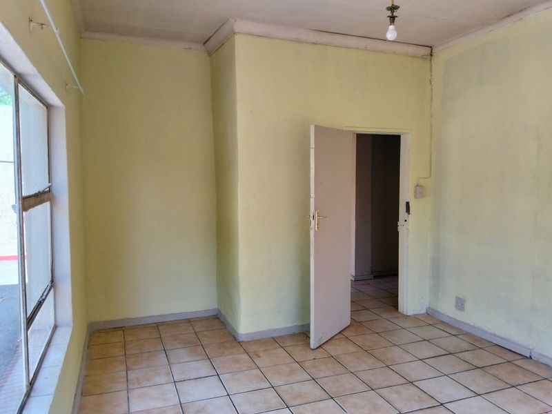 An empty bedroom featuring ceramic floor tiles, coved ceilings, and a single-pane window, offering a blank canvas for renovation.