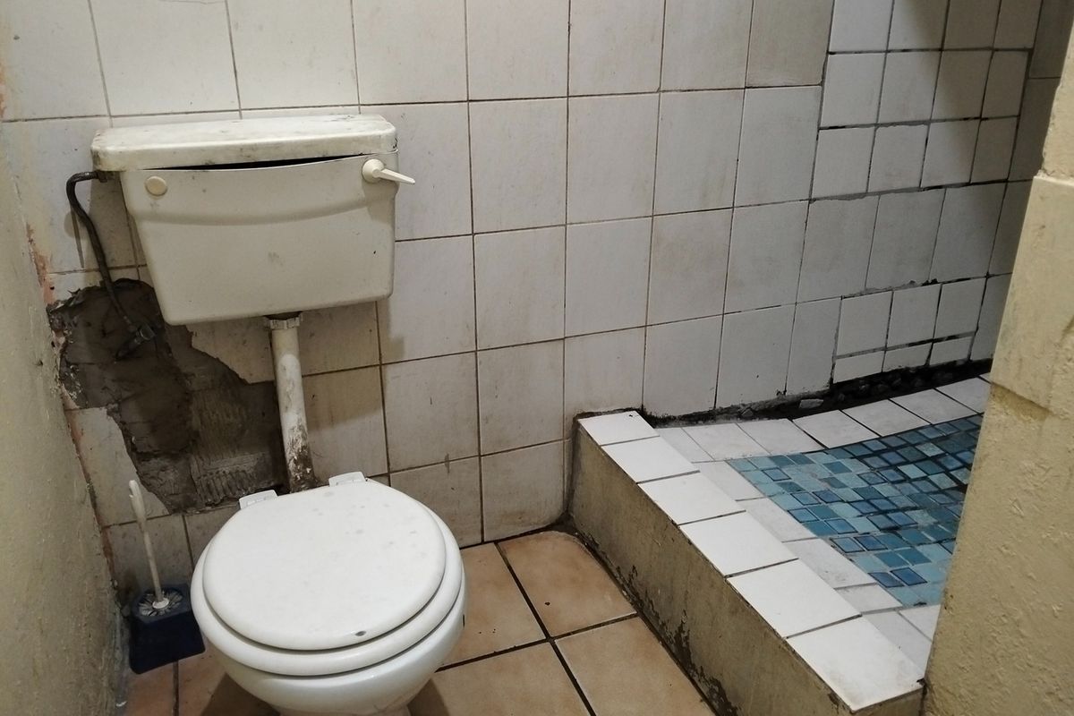A bathroom featuring a toilet and a raised shower base, currently requiring significant renovation and repair to the wall tiling and plasterwork.