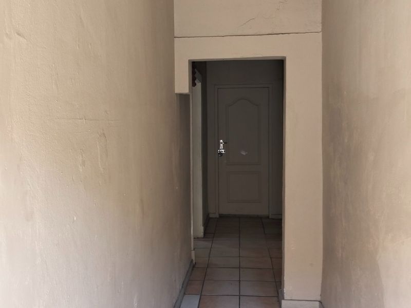 A narrow hallway featuring tiled flooring and decorative ceiling cornicing, showing signs of wear on the wall surfaces.