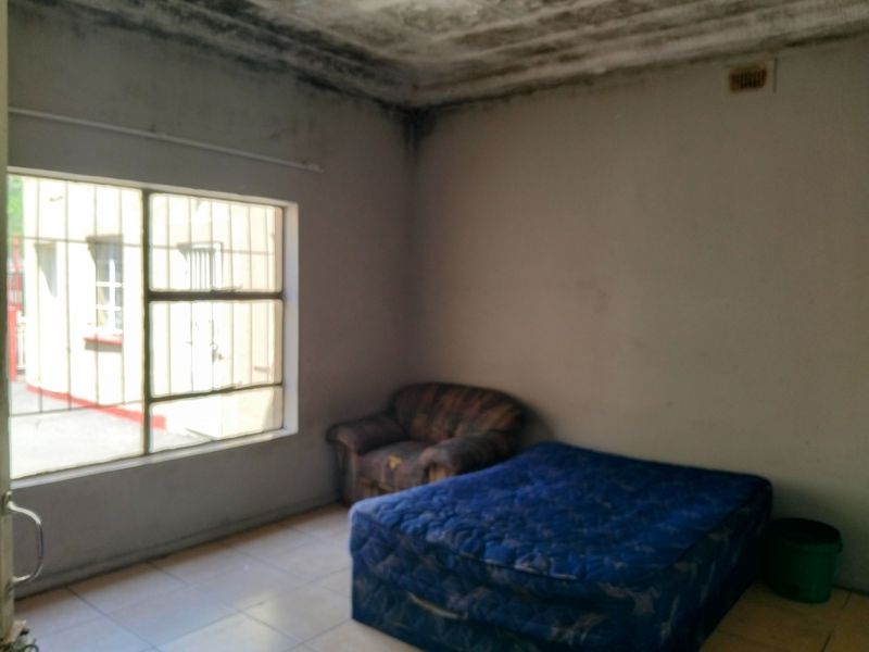 A bedroom featuring tiled flooring and security bars on the window, currently showing significant signs of ceiling and wall deterioration.