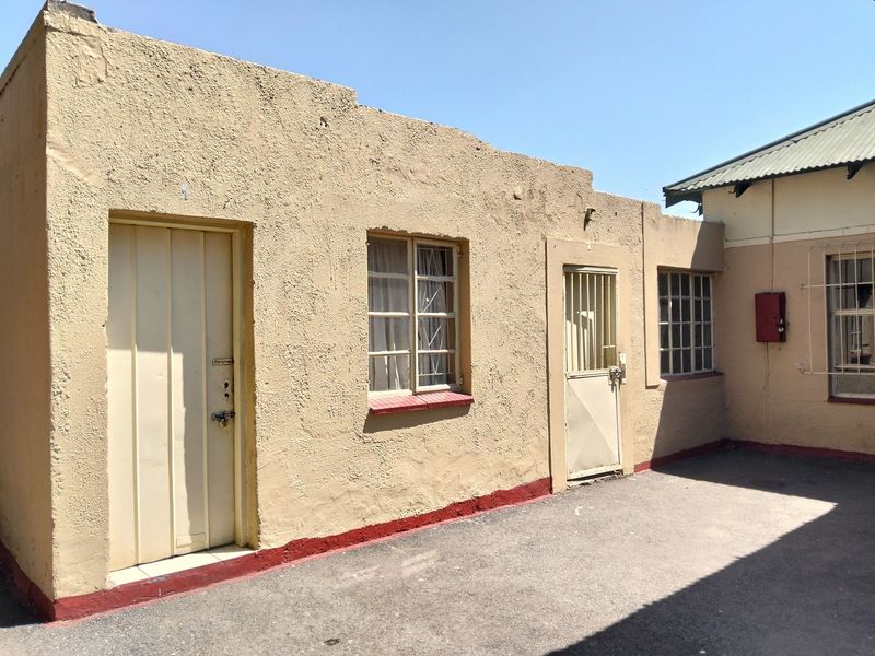 Rear exterior view of the property featuring a textured stucco facade, security gates, and paved outdoor area.
